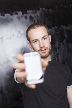 Man showing screen of smartphone, black t-shirt and background, studio shotの写真素材