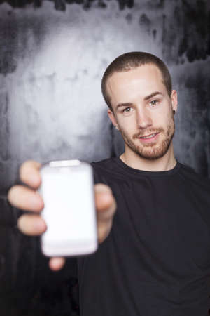 Men showing screen of smartphone, focus on face, black t-shirt and background, studio shotの写真素材
