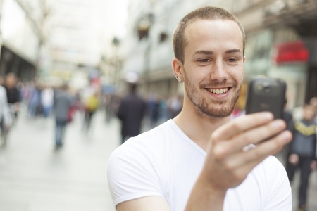 Young Man with mobile phone walking, background is blured cityの写真素材