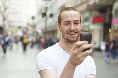 Young Man with mobile phone walking, background is blured cityの写真素材