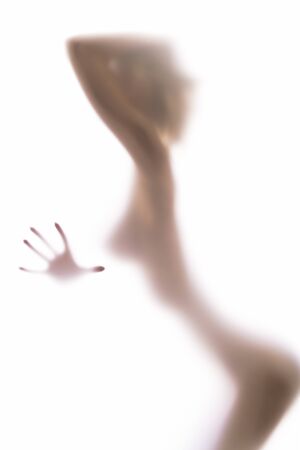 Blurred glass of bathroom hiding sexy female silhouette, one hand fingers in focusの写真素材