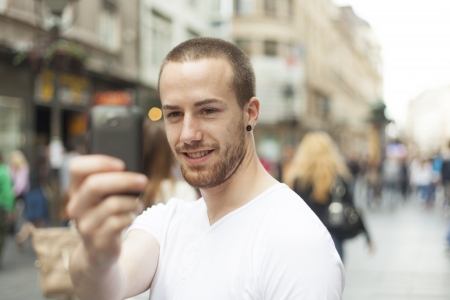 Guy on street photographing with mobile phone, background is blured cityの写真素材
