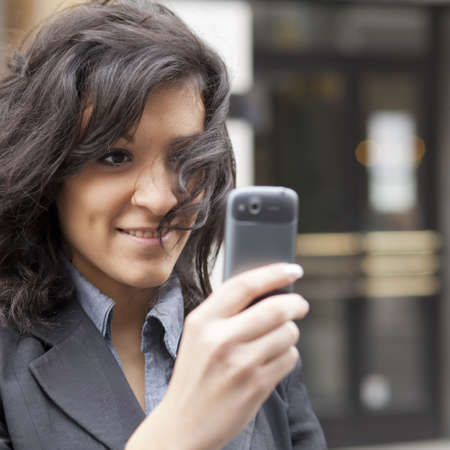 Young Woman photographing with mobile phone, background is blured buildingの写真素材