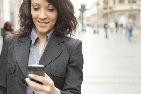 Young Woman with cellphone walking on street, downtown. In background is blured streetの写真素材