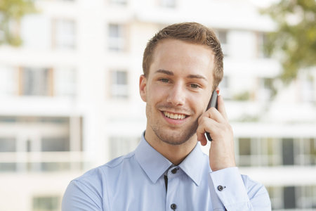 Smiling Businessman with smart phone on hand, blurred backgroundの写真素材