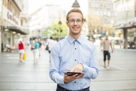 Young businessman with glasses and tablet computer on streetの写真素材