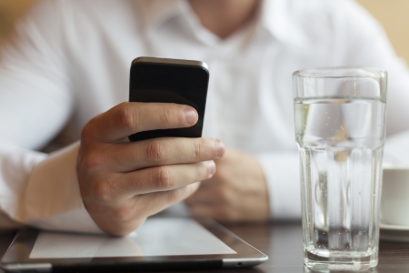 Man with smart phone in hand, blurred background, glass of watherの写真素材