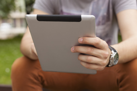 Young man read news and communicate on social networks with tablet computer in park