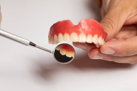 Denture prosthesis in doctor orthodentist dentist hand, checking with mirrorの写真素材