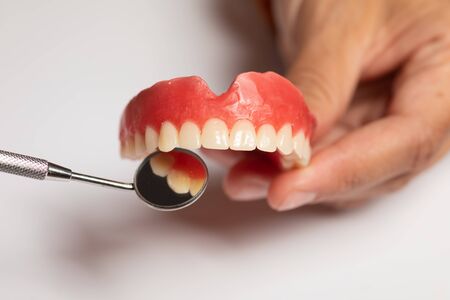 Denture prosthesis in doctor orthodentist dentist hand, checking with mirrorの写真素材
