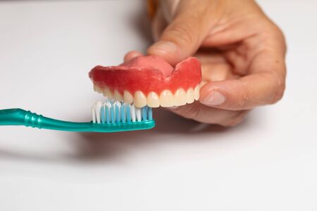 Oran hygiene: Doctor dentist show how to Cleaning dental prosthesis with toothbrush, hold denture in...