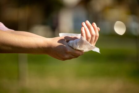 Cleaning hands with antibacterial wet wipes outdoor against disease infection versus flu or infulenza, blurred green backgroundの写真素材