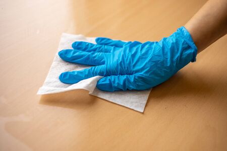 Woman's hand in blue gloves sanitizing cleaning home office wood table surface with wet wipesの写真素材
