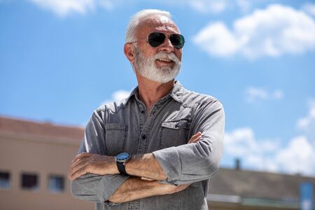 Rich old man with beard and sun glasses on street posing and smiling, portrait