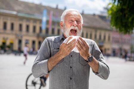 Old man coughs and sneezes into a handkerchief on street, outdoor, hot summer, allergies and illness...