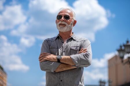 Old rich man with beard and sun glasses on street posing and smiling, portraitの写真素材