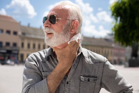 Old man cleaning neck and sweat with wet wipes on street on hot summer day, blurred urban city...
