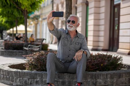 An older tourist man enjoys a vacation and takes a selfie on the street