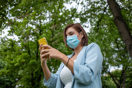 Woman with blue face mask using phone outdoor stock photoの写真素材
