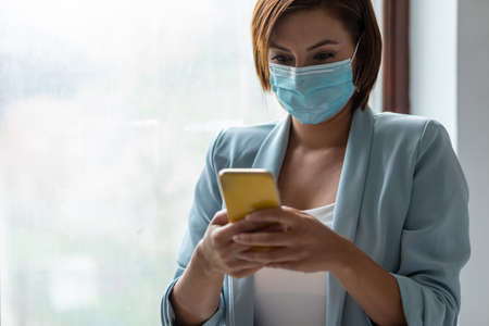 Woman with face mask using smartphone indoor