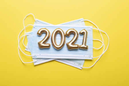 Gold numbers 2021 with face mask on yellow background. Happy new pandemic year