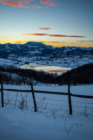 Colorful sunset evening at mountain lake Rovni in snow, beautiful nature winter scene in Serbiaの写真素材