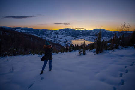 Photographers photographing winter lake mountain scene in sunset, alone in wilderness. Rovni, Valjevo, Serbiaの写真素材