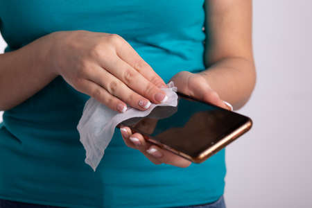 Woman holding and cleaning sanitizing phone smartphone with wet wipesの写真素材