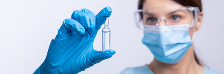 Doctor in protective gloves and mask holding glass vial with injection liquid.