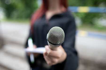 Female journalist at news conference, writing notes, holding microphoneの写真素材