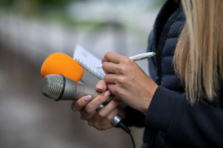Female journalist at news conference, writing notes, holding microphoneの写真素材