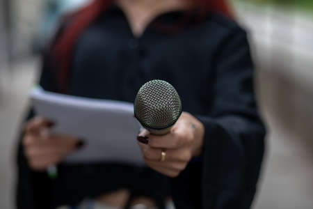 Loud and clear! Female journalist at news conference, writing notes, holding microphoneの写真素材