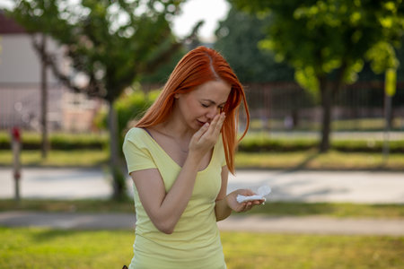 Hard simptops of allergy. Young redhair woman sneezing in front of blooming tree. Pollen Allergy symptomsの写真素材