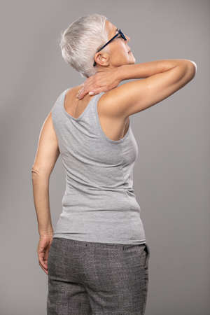 Backache pain in back, senior old woman with short gray hair and body and spinal muscle problemsの写真素材
