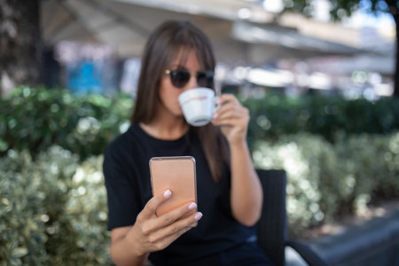 Morning in cafe - attractive woman in black dress and dark sun glasses drinking coffee and make selfie photo for social networks. stock photoの写真素材