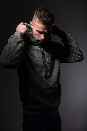Young worried man looks away, studio portrait, dark gray background