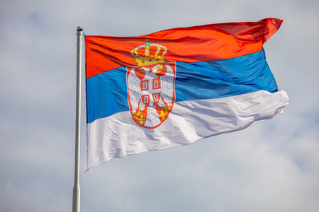 Serbian national flag on wind, outdoor, cloudy backgroundの写真素材
