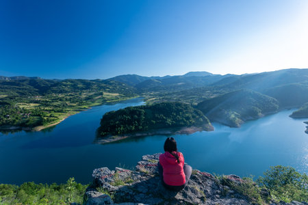 A Woman Sitting On A Rock Looking Out Over A Beutiful Nature Scene. A Beautiful View Of A Lake And...