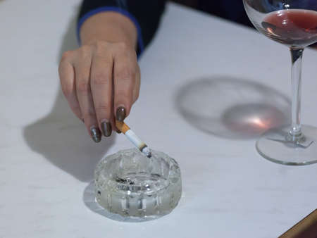 female hand with a cigarette over an ashtray near a glass of wineの写真素材