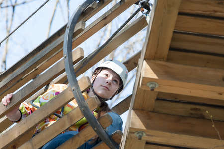 the girl climbs obstacles of rope park in clear summer day