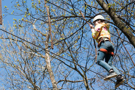 the girl climbs obstacles of rope park in clear summer day