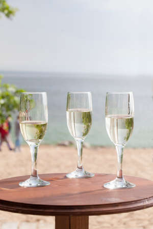 three glasses with champagne on a table against the beachの写真素材