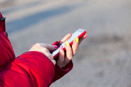 the woman in a red jacket dials number on phone in clear dayの写真素材