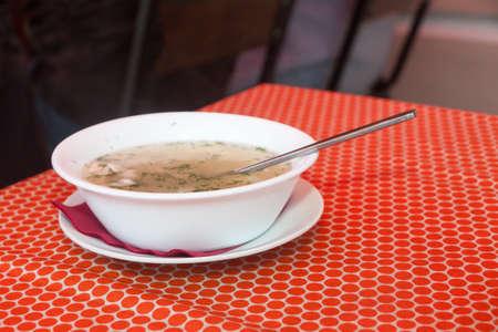 chicken soup in a white plate on a red cloth on a little table in cafeの写真素材