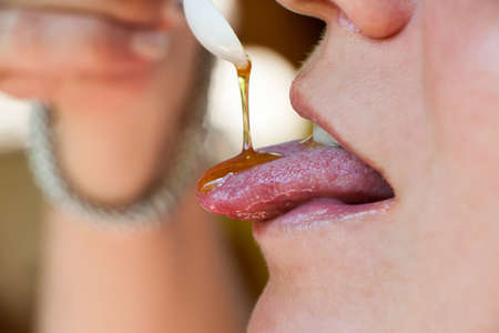 the honey which is flowing down in a mouth of the beautiful girl on tastings