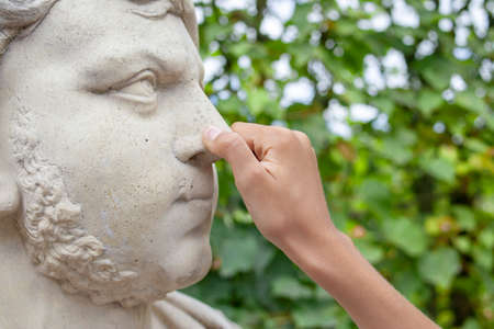 Hand of the boy holding by a nose a statue in summer day
