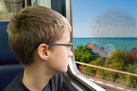 the young boy looks out of the window of the going train in clear summer day