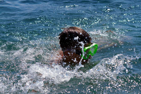 the teenager swims in a mask in the blue sea in clear summer day
