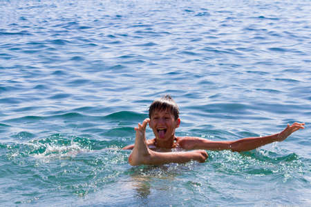 the teenager swims in the blue sea in clear summer day