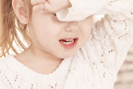 close-up portrait of a three-year-old whining girl in a light dressの写真素材